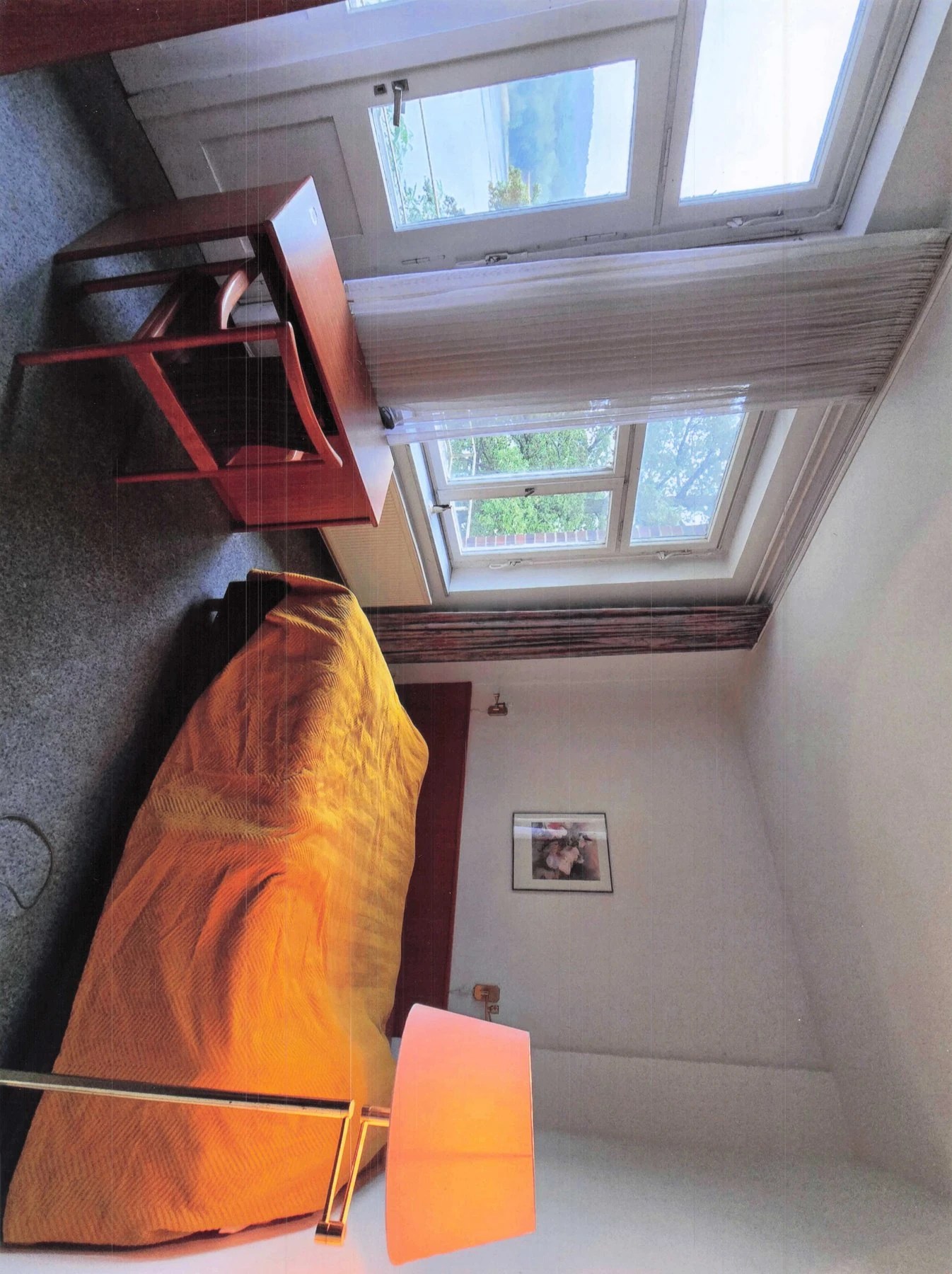 Zimmer mit Dachschräge, oranger Tagesdecke und Dachflächenfenster